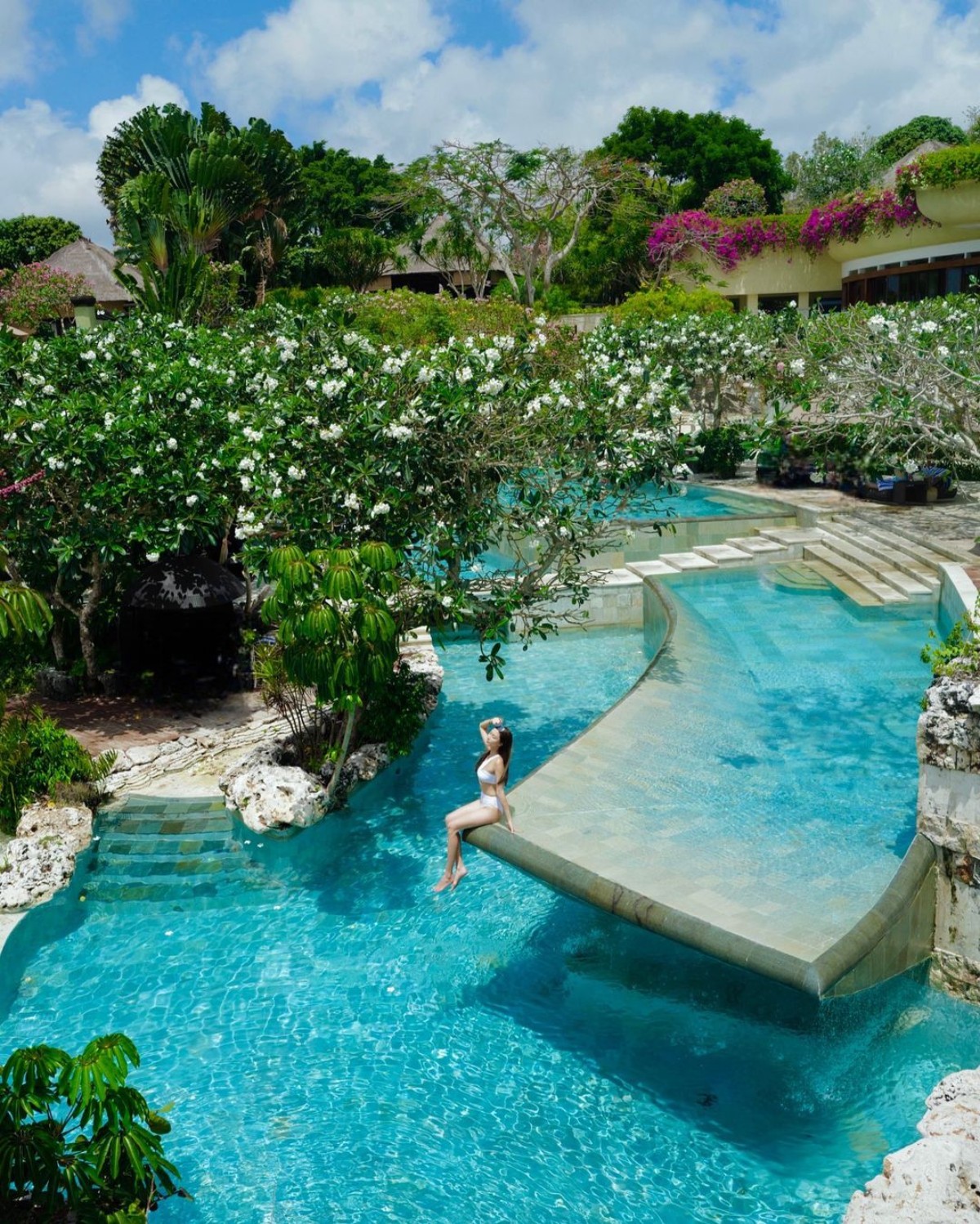 Lush gardens surround a tiered pool with a person resting on its edge in Ubud, Bali.