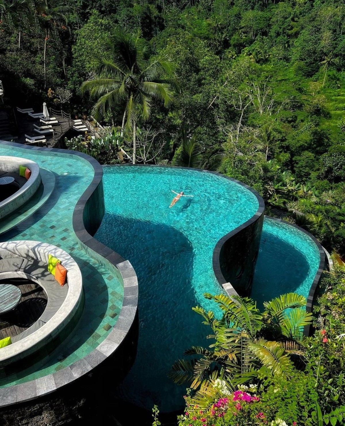 An azure pool winding through a jungle backdrop, with a lone swimmer floating amidst the tranquility in Ubud, Bali.